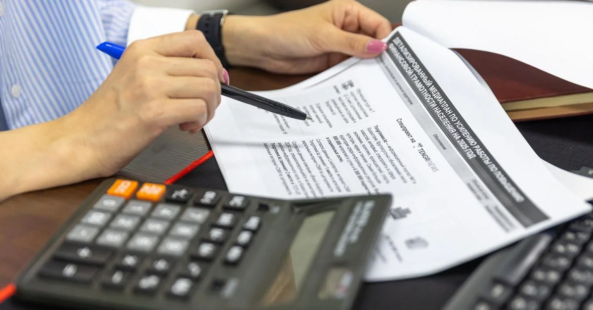 primer plano de una persona analizando documentos financieros con una calculadora y un bolígrafo.