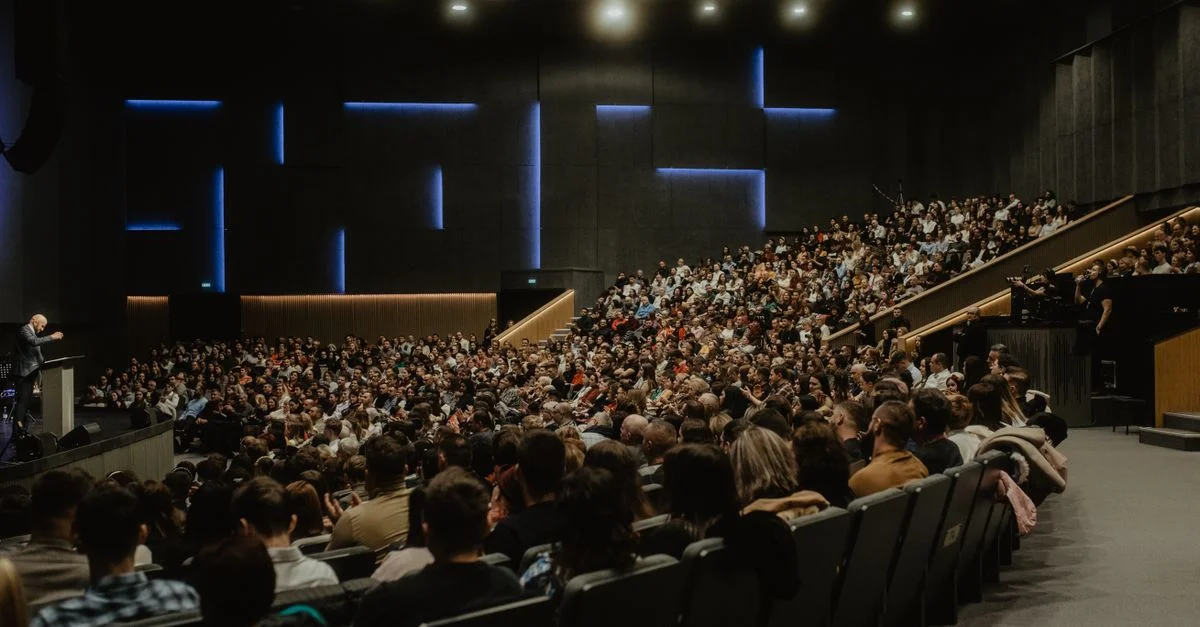Una gran audiencia escucha atentamente a un ponente en una conferencia en Oradea, Rumanía.
