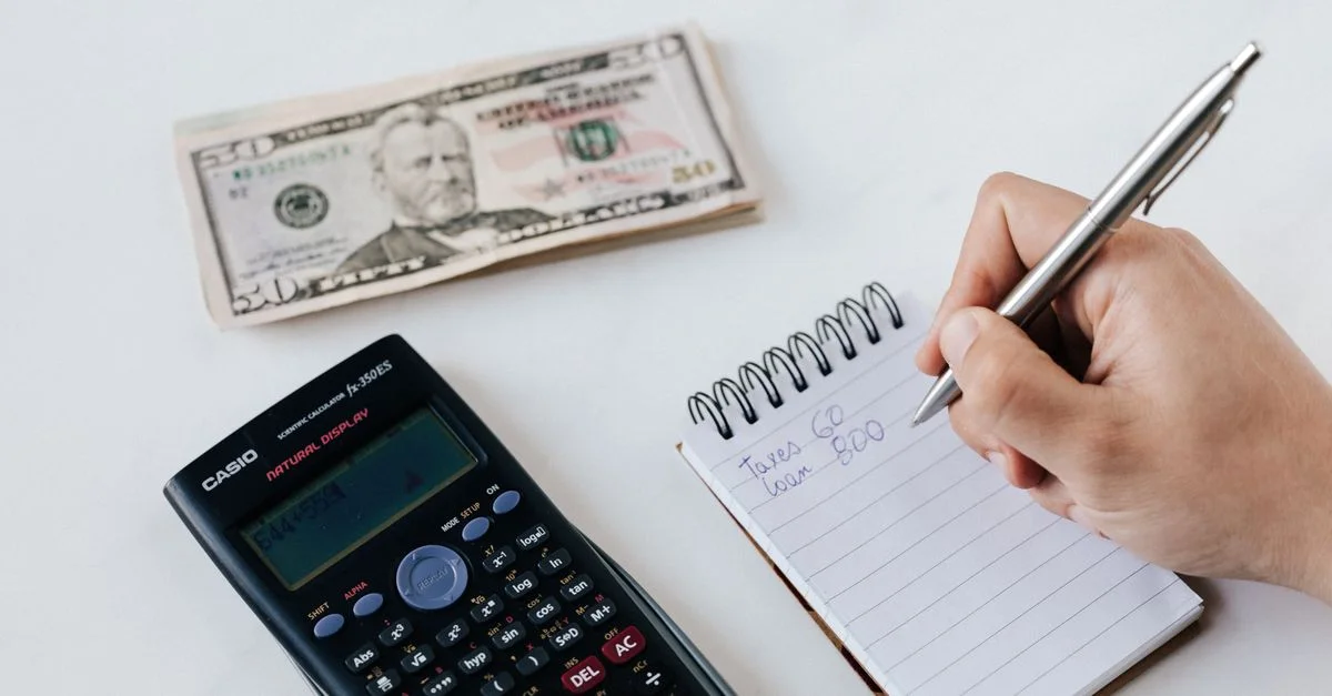 Primer plano de artículos de presupuesto que incluyen calculadora, efectivo y cuaderno para planificación financiera.