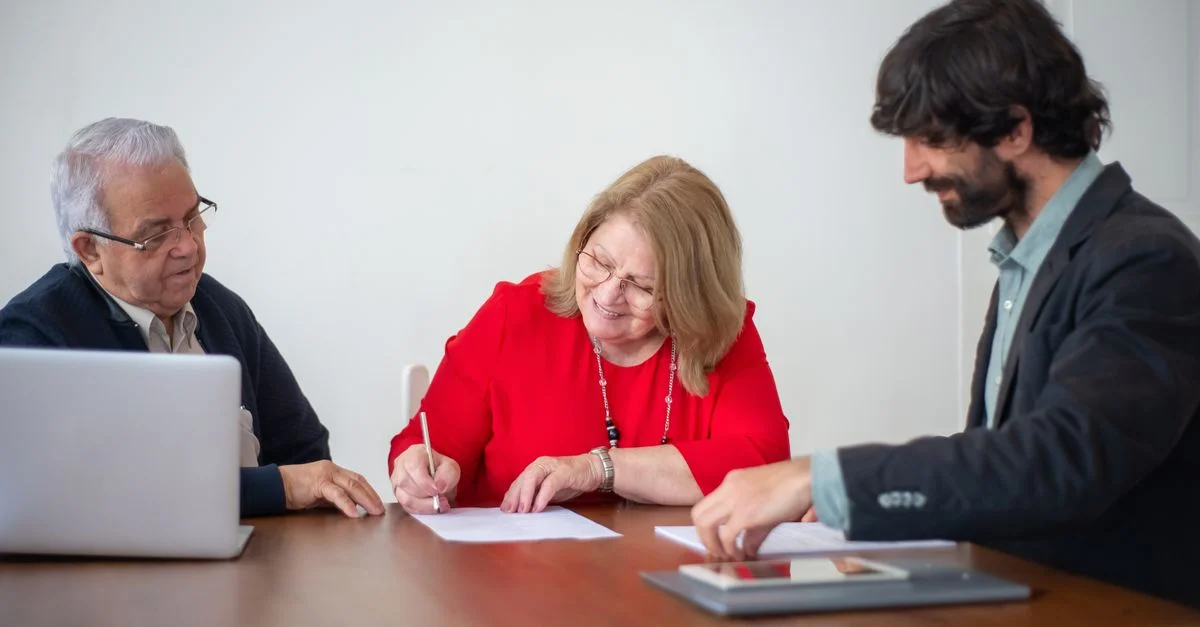Profesionales de negocios senior firmando documentos durante una reunión en una oficina iluminada.