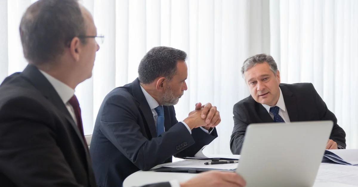 Tres hombres de negocios colaborando durante una reunión alrededor de un portátil en una oficina brillante.