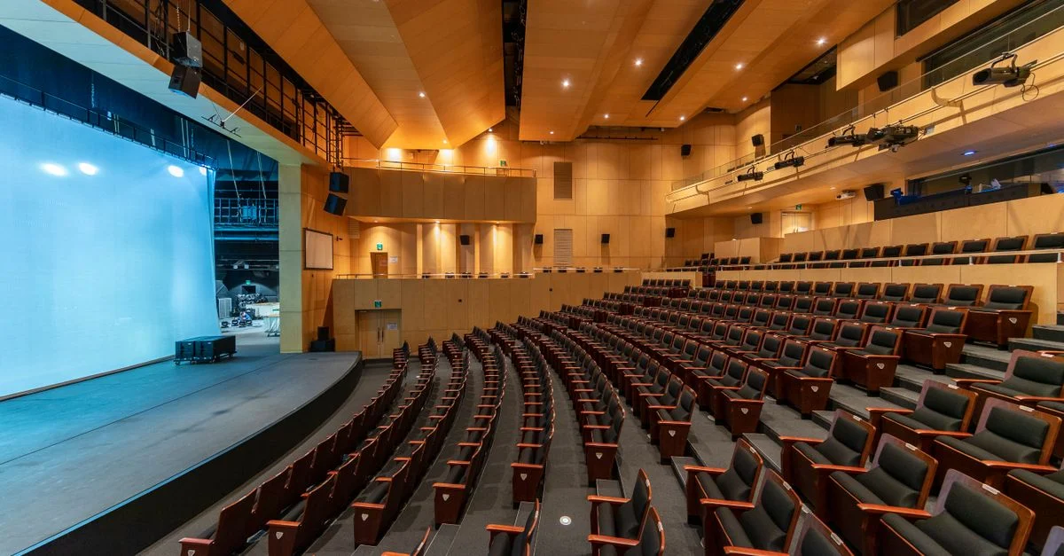 Amplio auditorio contemporáneo con asientos vacíos y un escenario, ideal para conciertos o presentaciones.